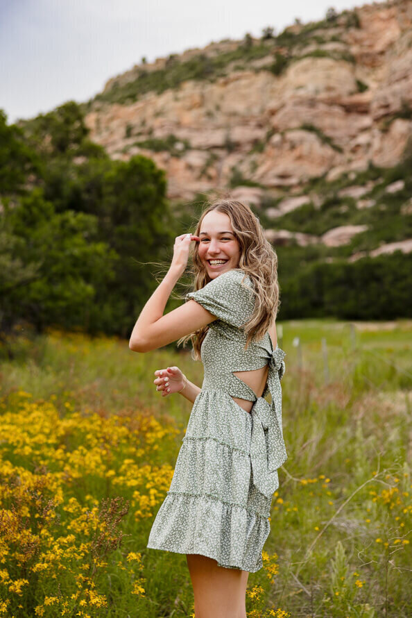 Girl laughs and fixes hair in a field of yellow flowers.