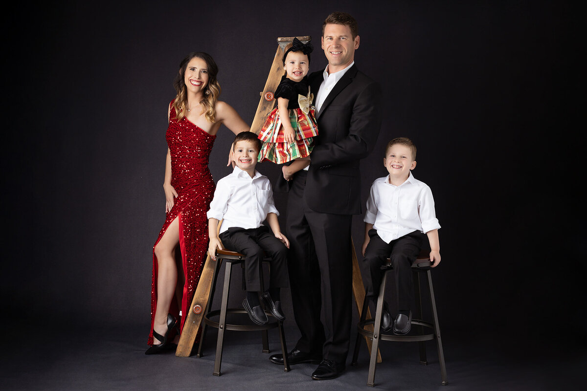 A family dressed in holiday attire, captured in a festive Dallas family portrait photographer session with a playful mood and a ladder prop.