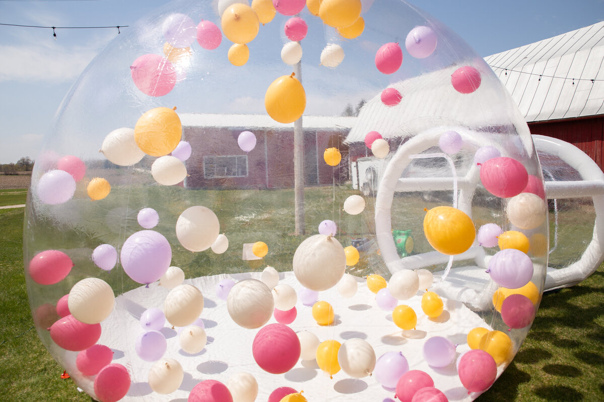 A giant transparent bubble with pink, orange, and purple balloons inside.