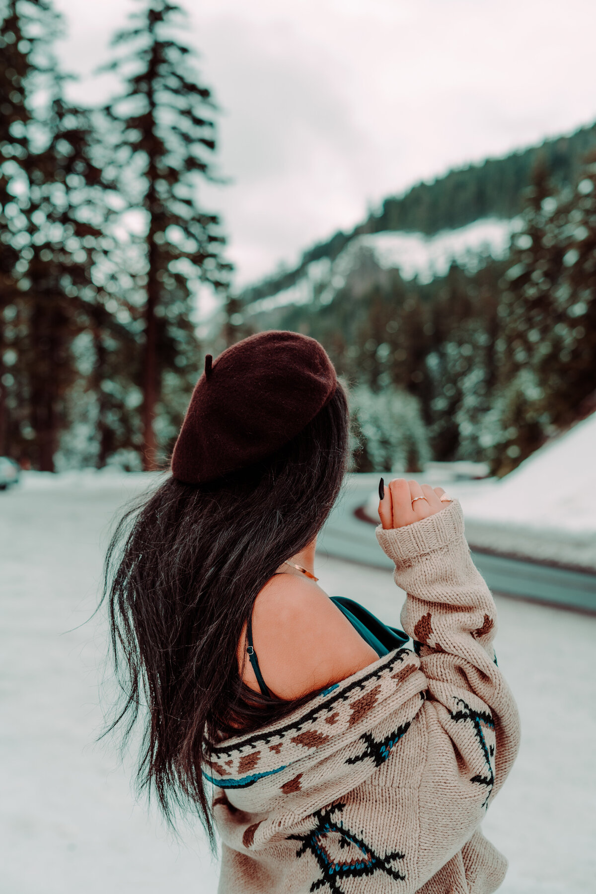 Woman standing with back turned in cozy sweater among pines – peaceful outdoor branding session by Mewphotovideo