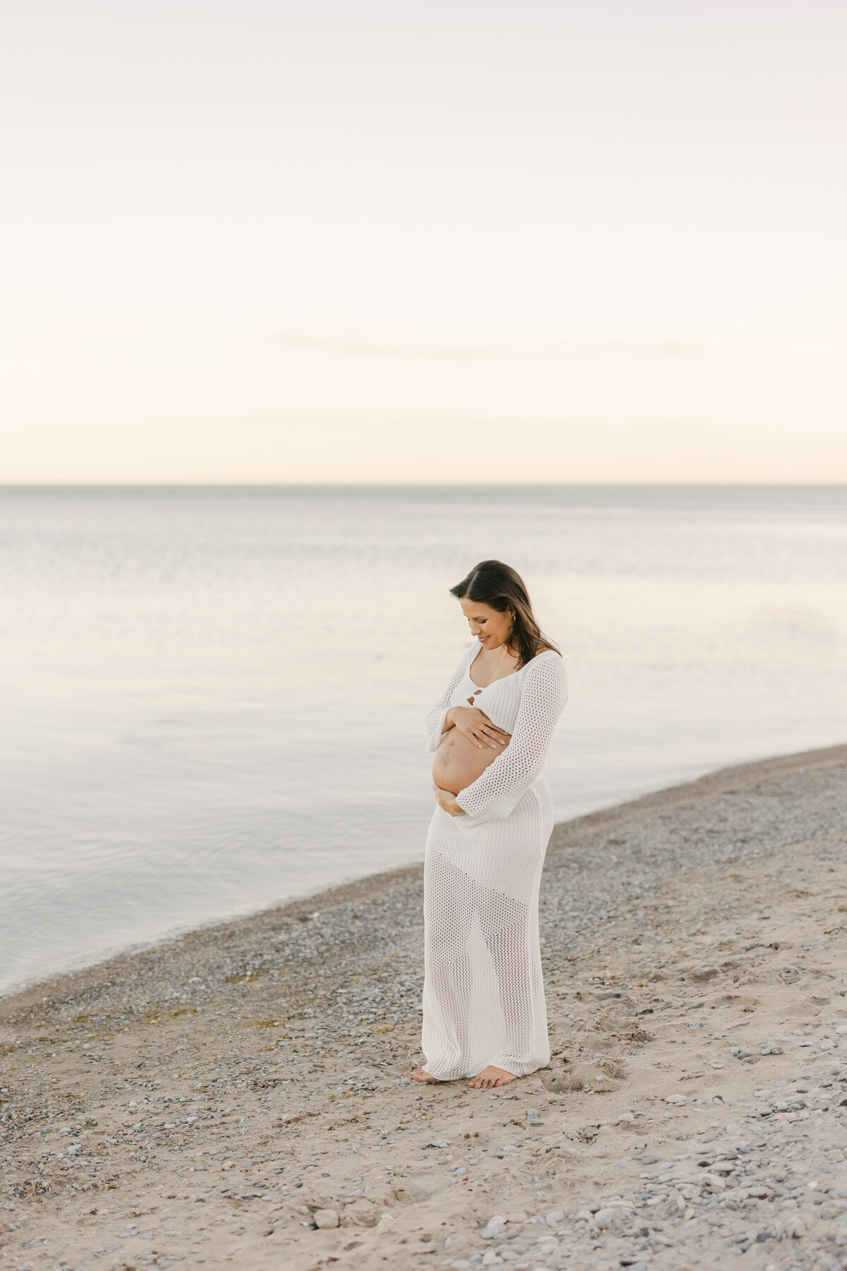 A pregnant mother looking and touching at her belly at a Toronto beach