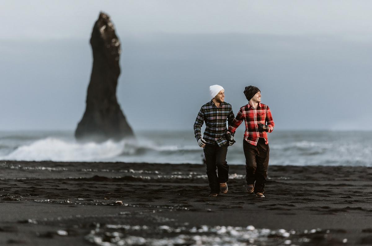 lgbtq+ photographer in iceland. groom and groom are running on the black sand beach