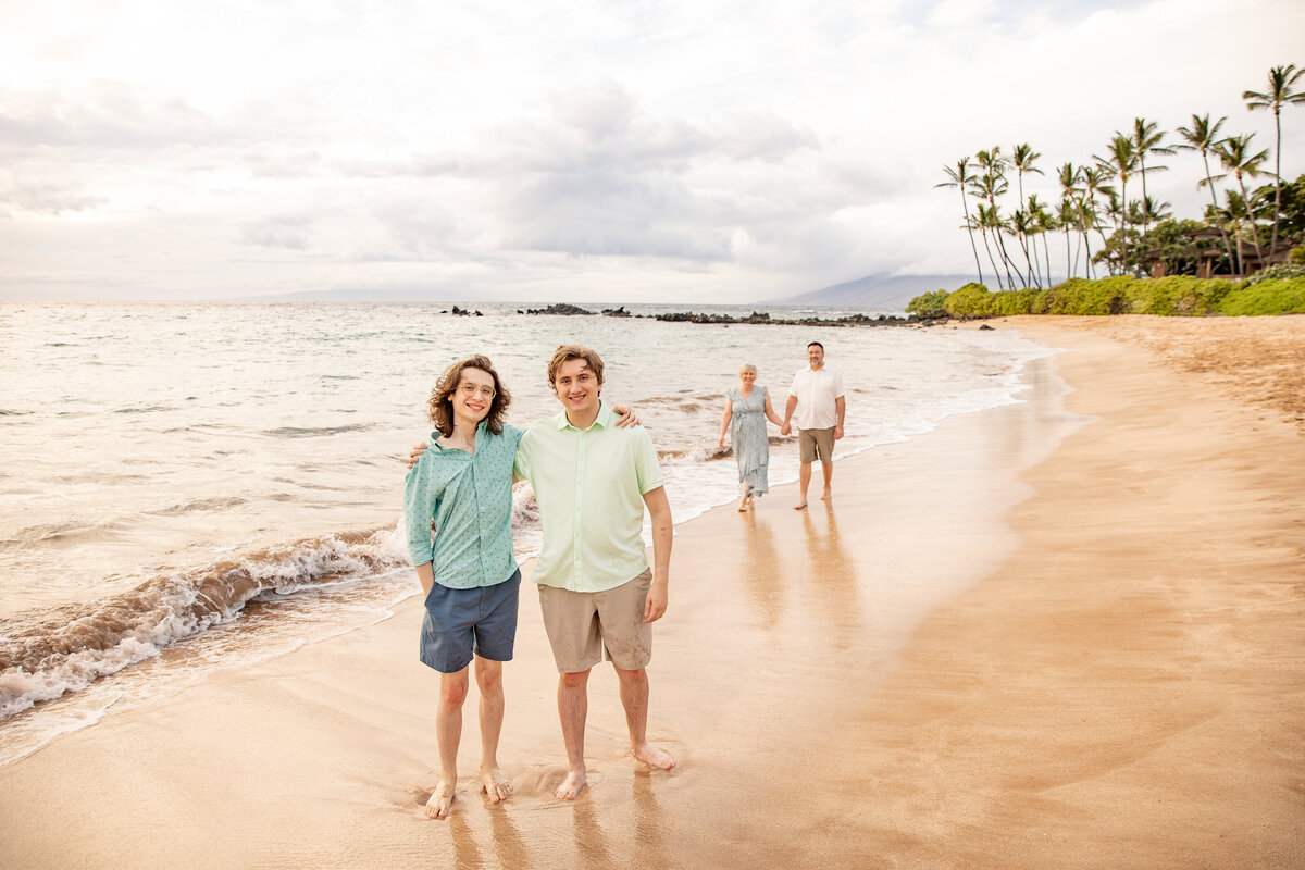 Maui Family Photographers capture sons smiling at camera while parents walk in background