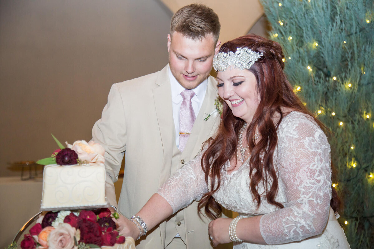 redheaded bride and groom in a cream suit cutting cake at their wedding reception