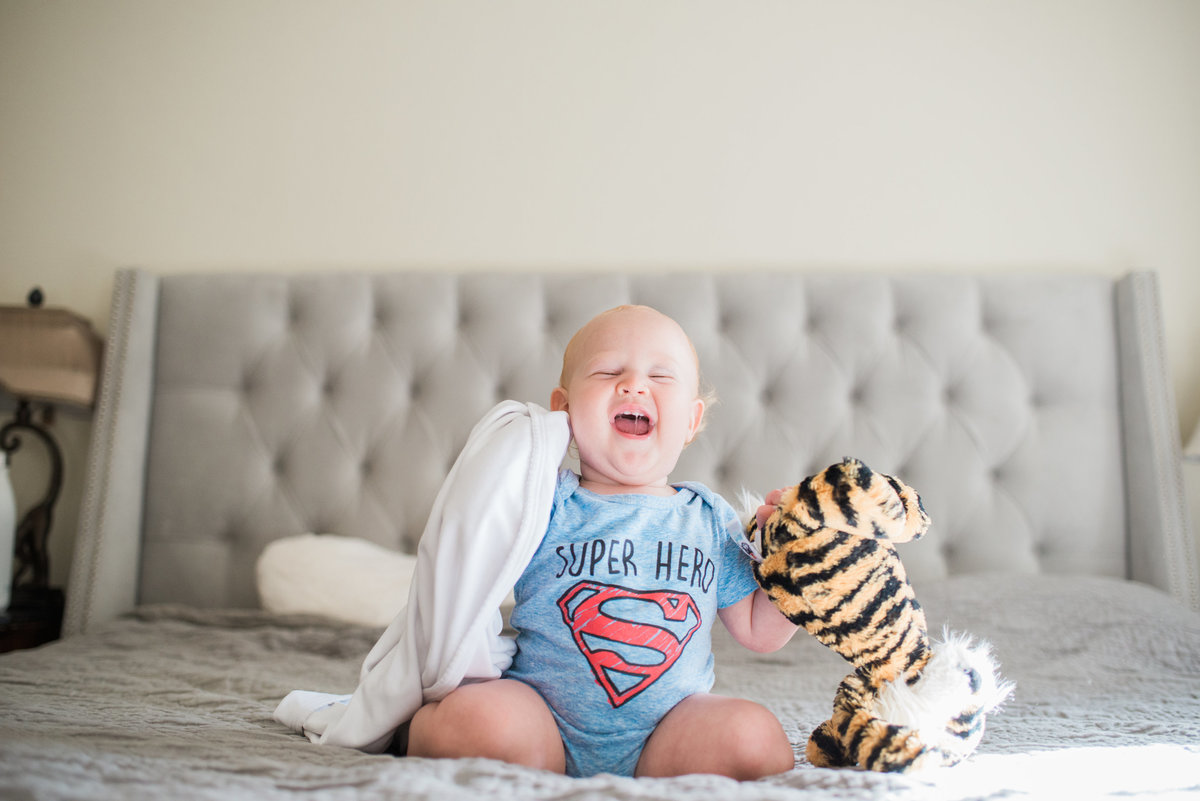 baby holding stuffed tiger and blanket laughing