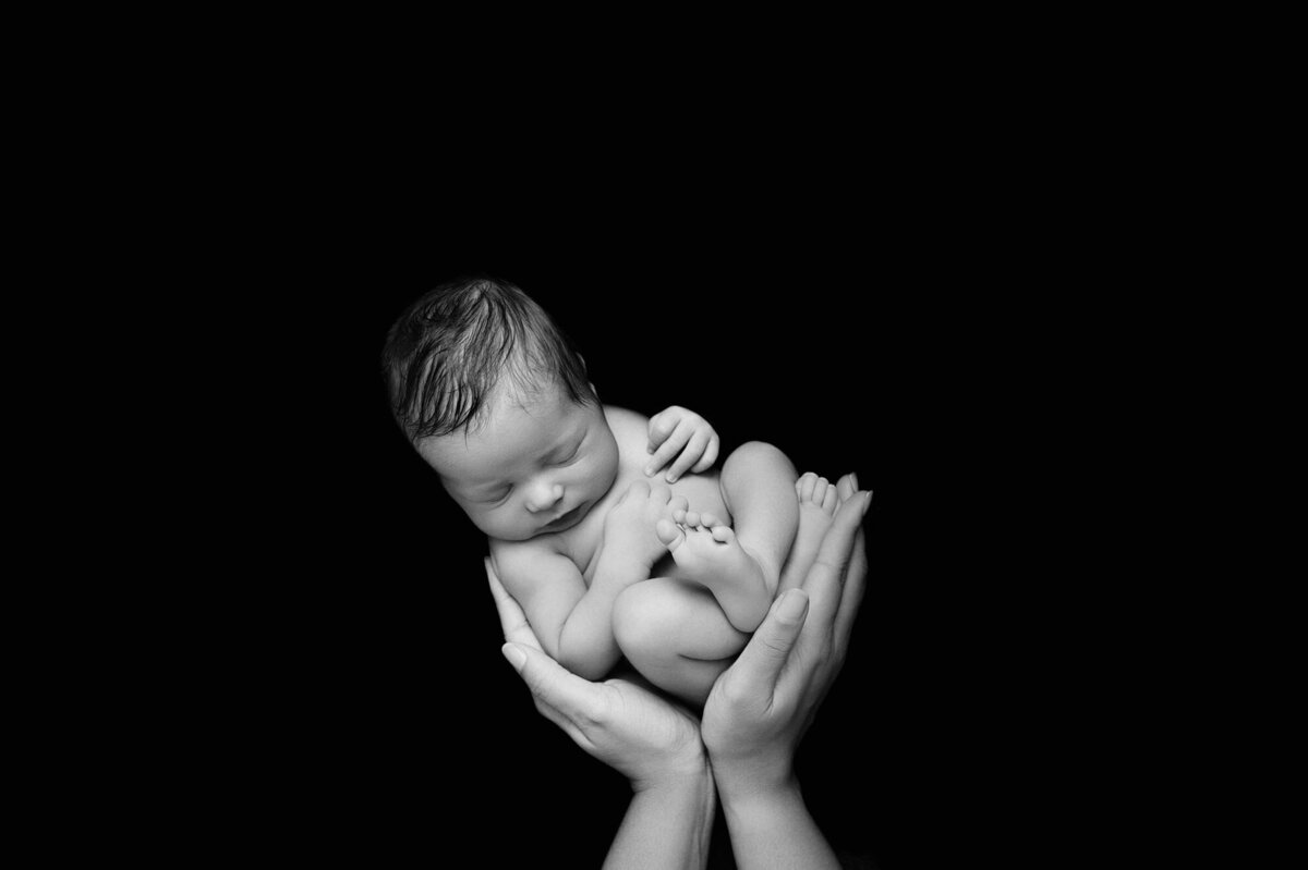newborn in moms hands photographed on black