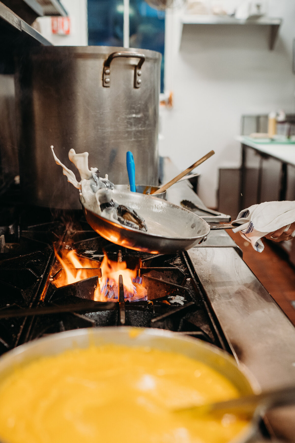 chef tosses mussels in pan over fire