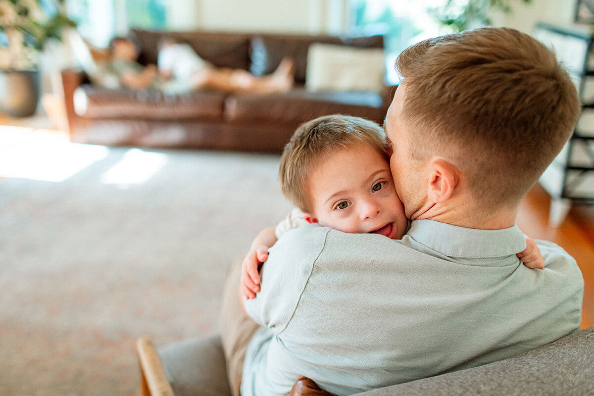Candid family moment of a child hugging their dad at home, captured by San Antonio photographer Sara James.