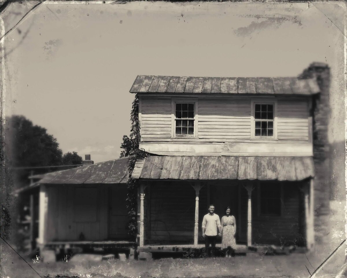 A couple stands in front of an old, weathered house