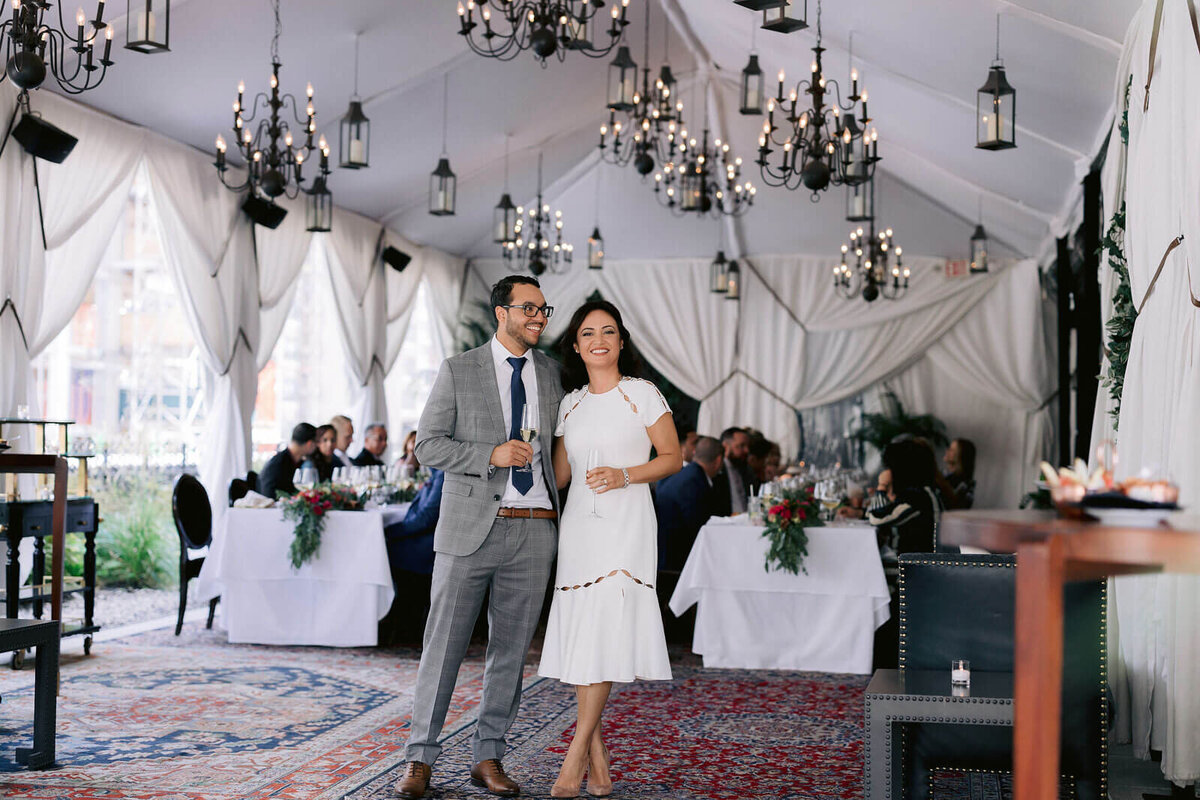 The bride and groom are happily standing inside the wedding reception venue in NYC while the guests are eating. Image by Jenny Fu Studio