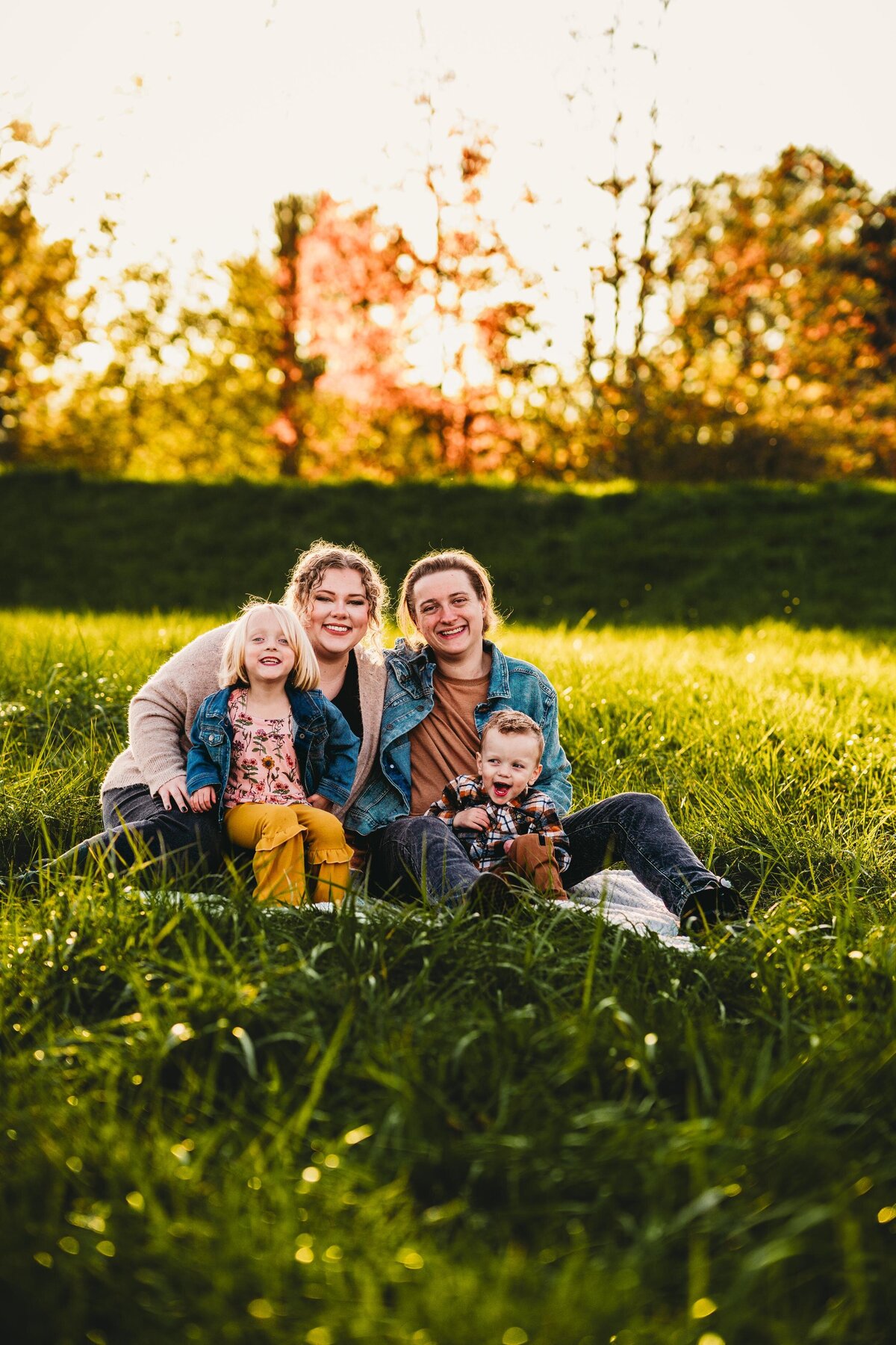 A happy queer family sits in a sunlit field during golden hour, sharing laughter and love.