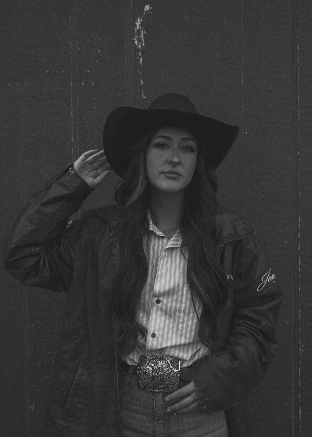 cowgirl poses and tips her hat while standing in front of a vintage barn in Bend, Oregon