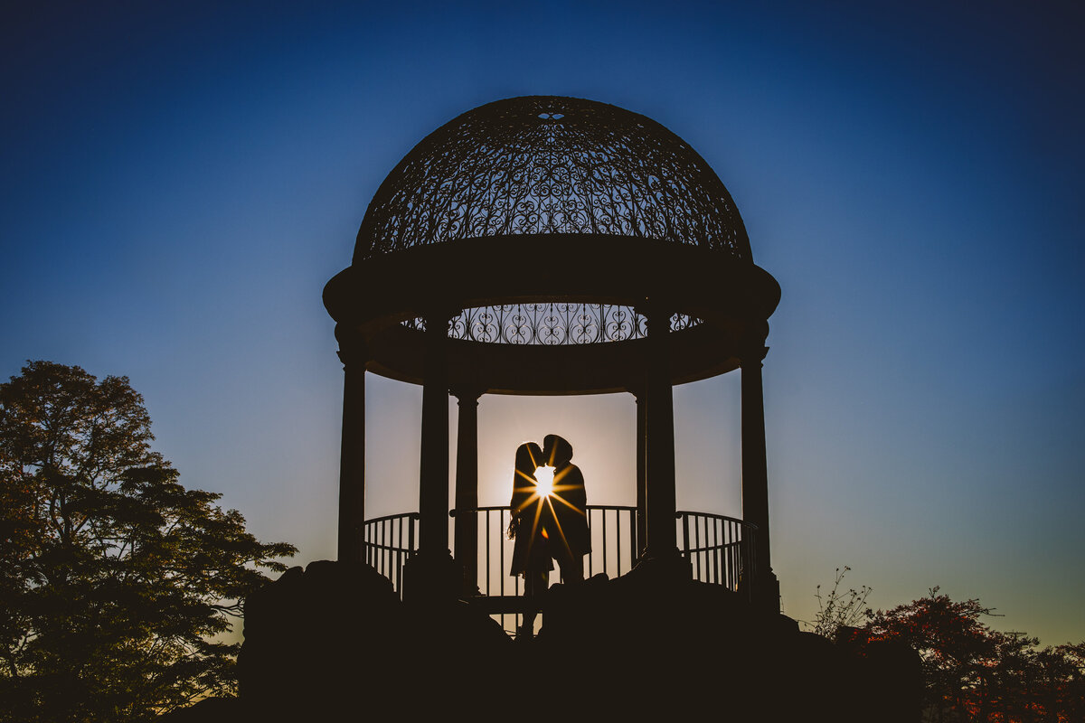 A silhouette of a couple kissing at sunset at the gazebo at untermyer gardens in yonkers