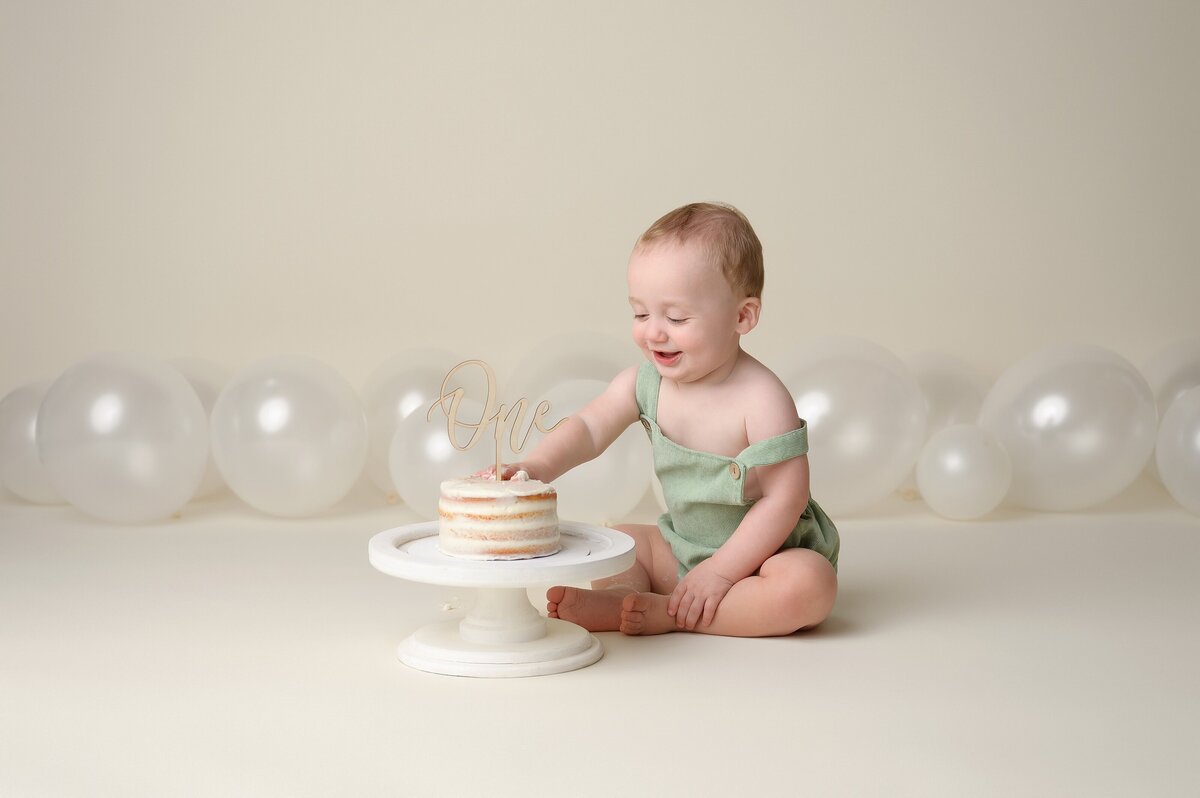 Baby celebrates first birthday eating a cake at his photoshoot in a timeless theme.