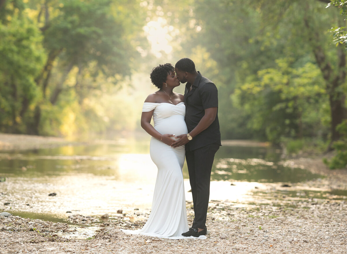 pregnant couple wearing black and white standing by a creek