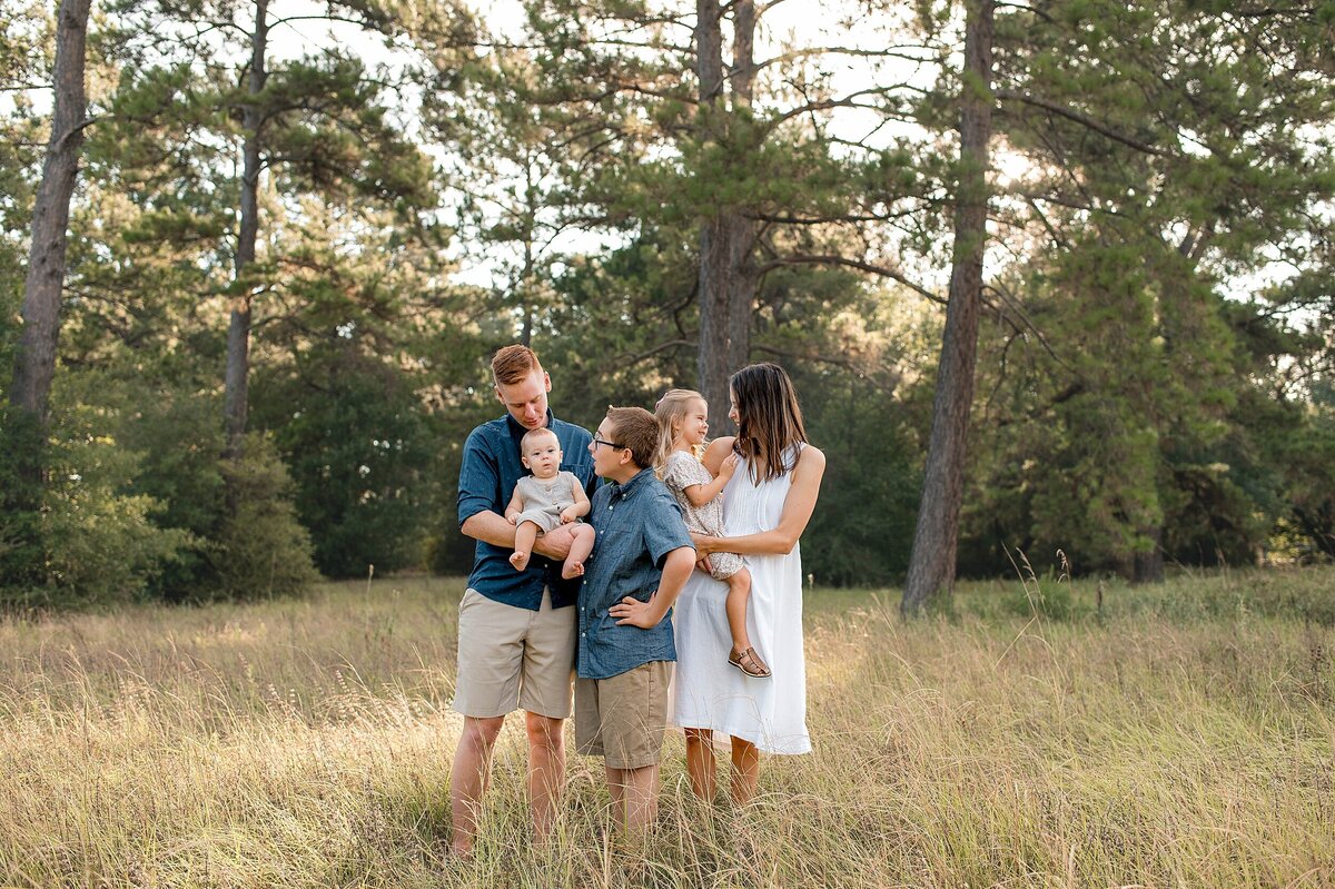 Family of 5 looking at each other smiling in a field by Cypress Family Photographer