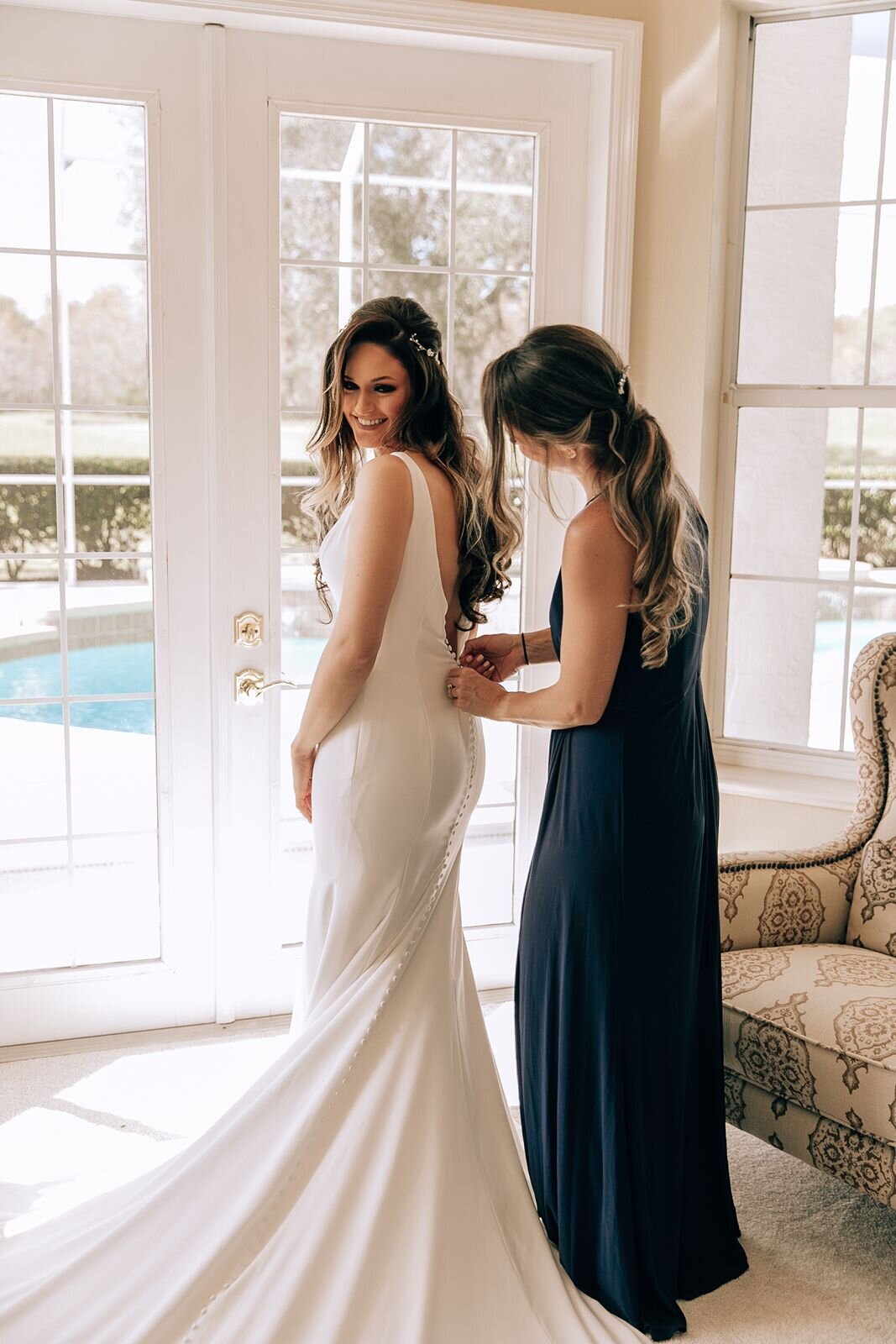 bride getting ready and her best friend zips up her dress