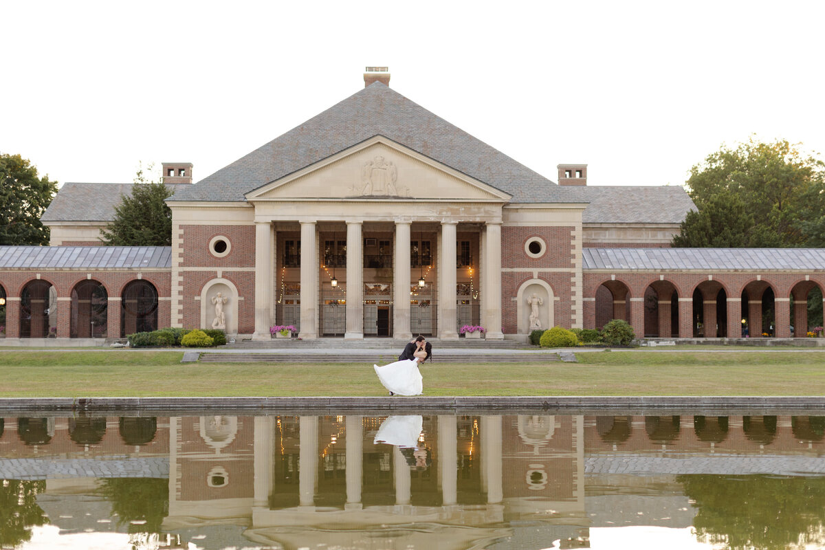 Bride and groom share a dip kiss in front of reflecting pond 