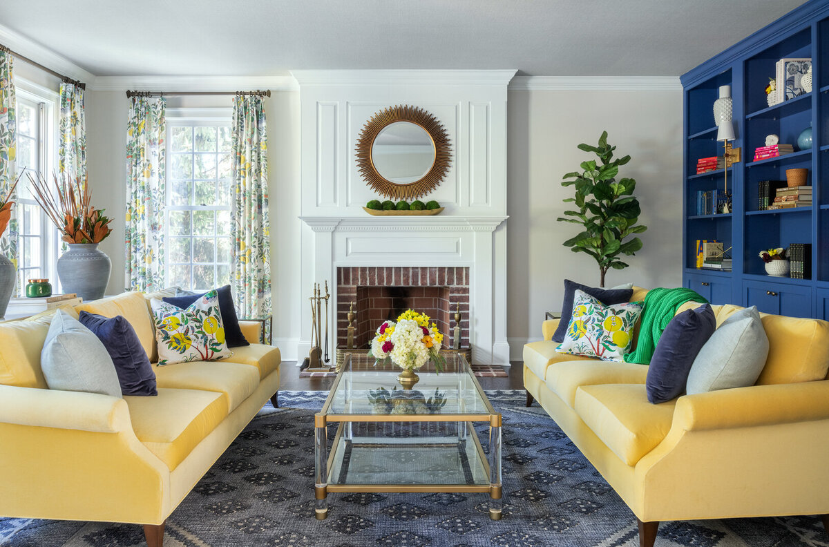 living room with two vibrant yellow sofas, blue built-in bookshelf in the right side and a white brick fireplace in the middle