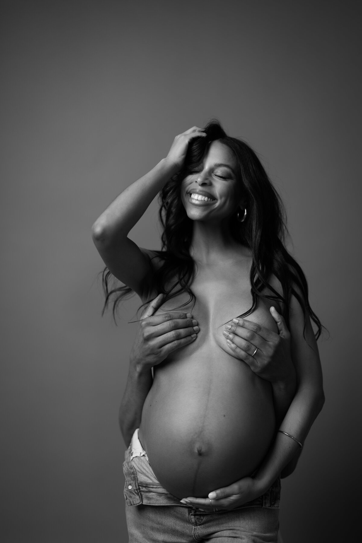 A black-and-white maternity portrait inspired by Janet Jackson's iconic Rolling Stone cover, capturing the expectant mother with a joyful smile and hands strategically placed, recreating a bold and empowering look.