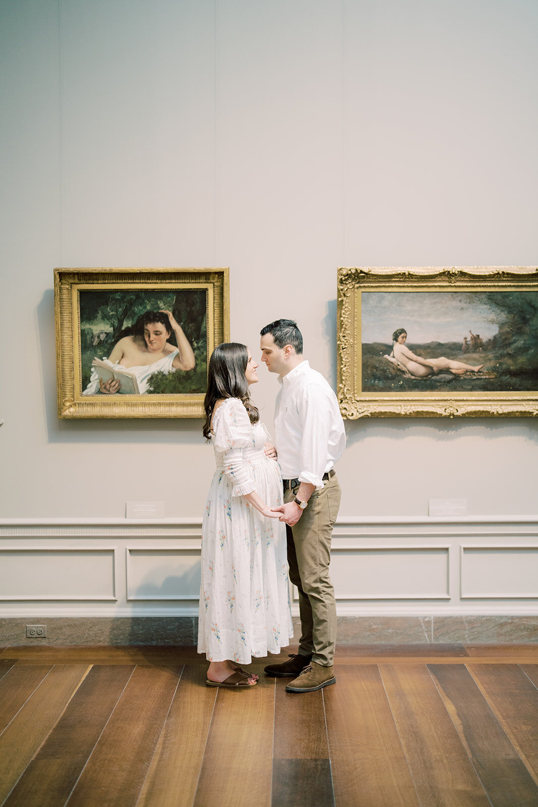 Pregnant mother stands holding her husband's hand and looking into each other's eyes in the National Gallery of Art.