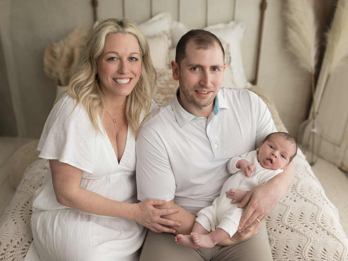 mom and dad holding newborn baby boy in white onesie for studio lifestyle session 