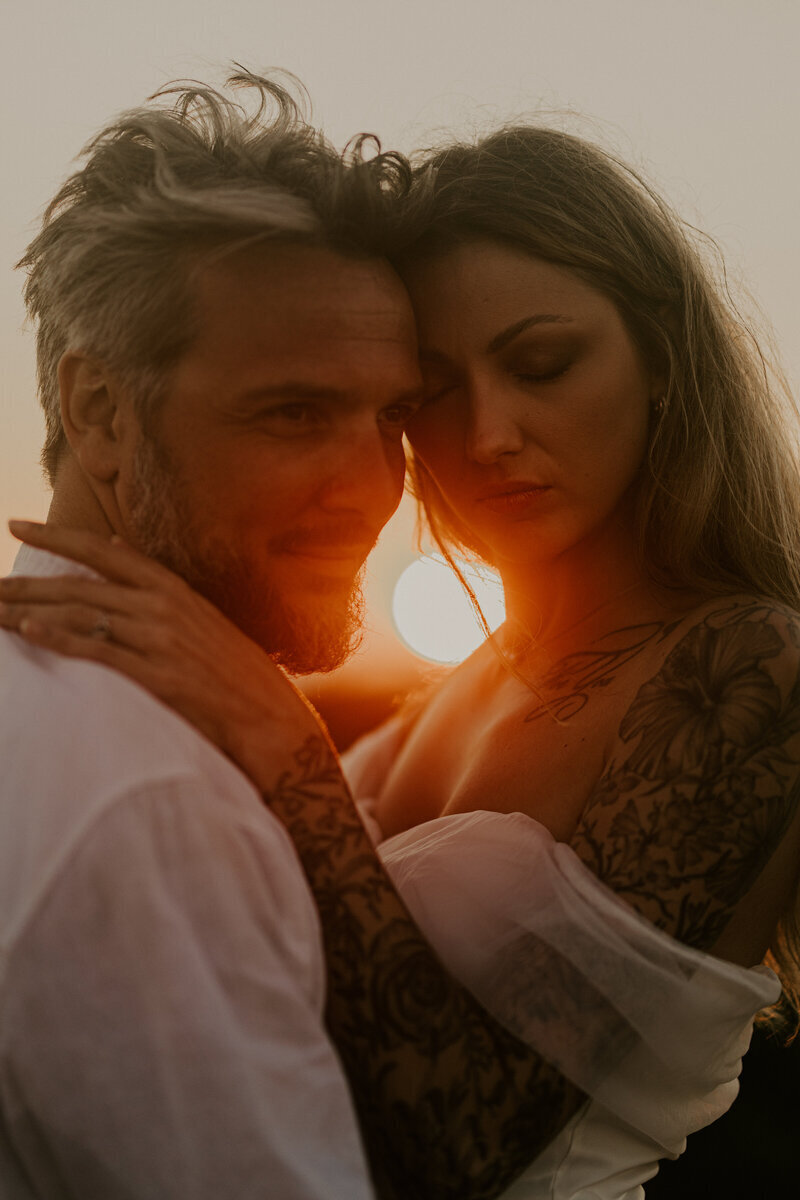 Couple enlacé, soleil rougeoyant perçant entre eux. Shooting photo à la plage en Vendée.