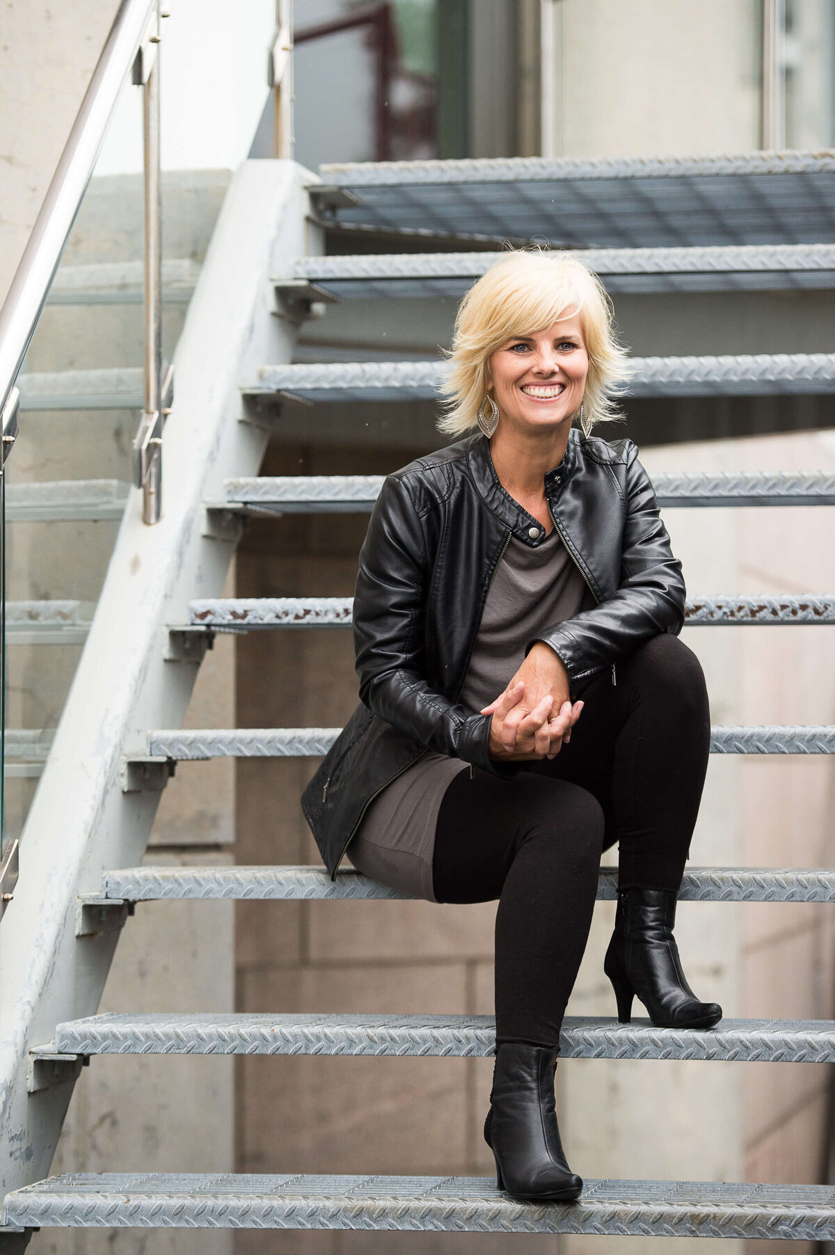 Ottawa branding photography of a woman in a leather jacket with blonde hair sitting on metal stairs in a city setting.  Captured outdoors by JEMMAN Photography COMMERCIAL