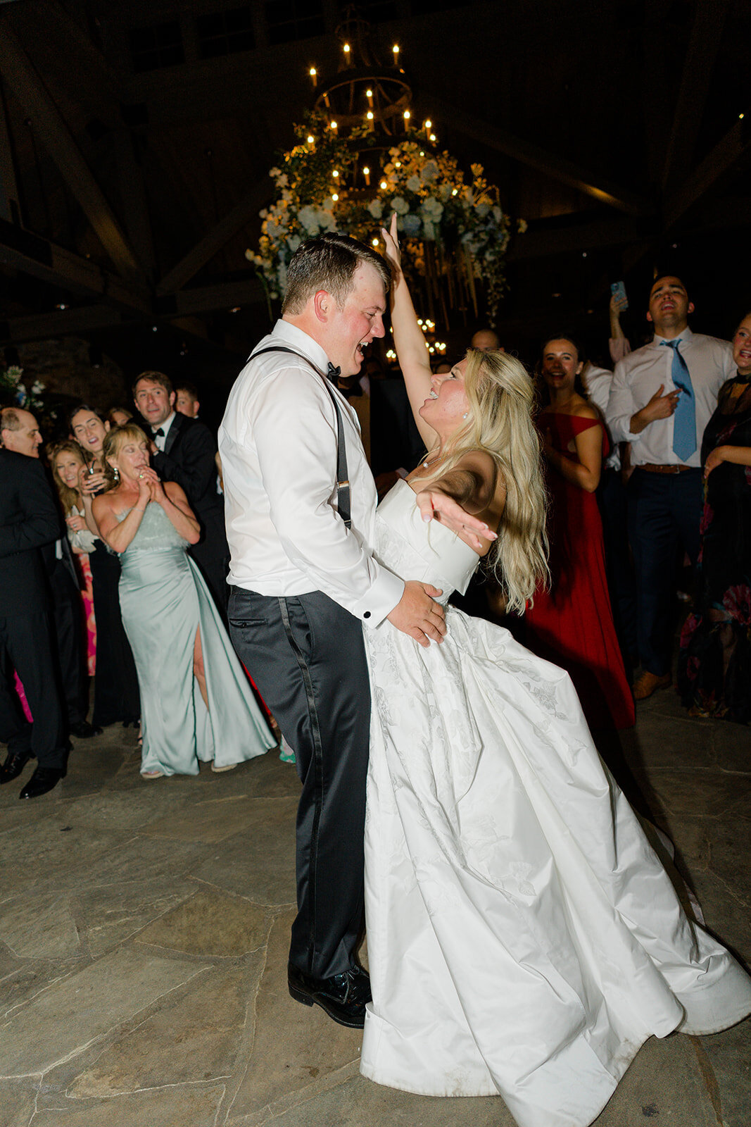 Bride and groom dancing surrounded by friends and family during a lively wedding reception.