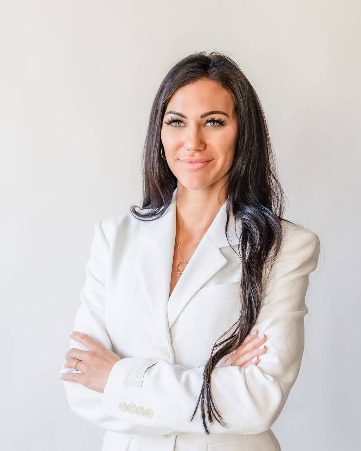 modern headshot of confident woman wearing white suit with long dark hair arms crossed