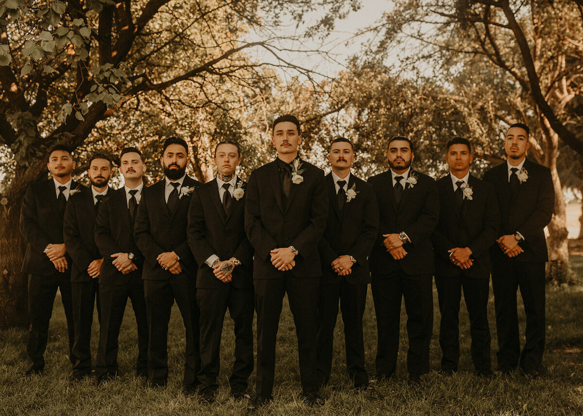 The groom and his men wearing their black suites and standing surrounded by trees