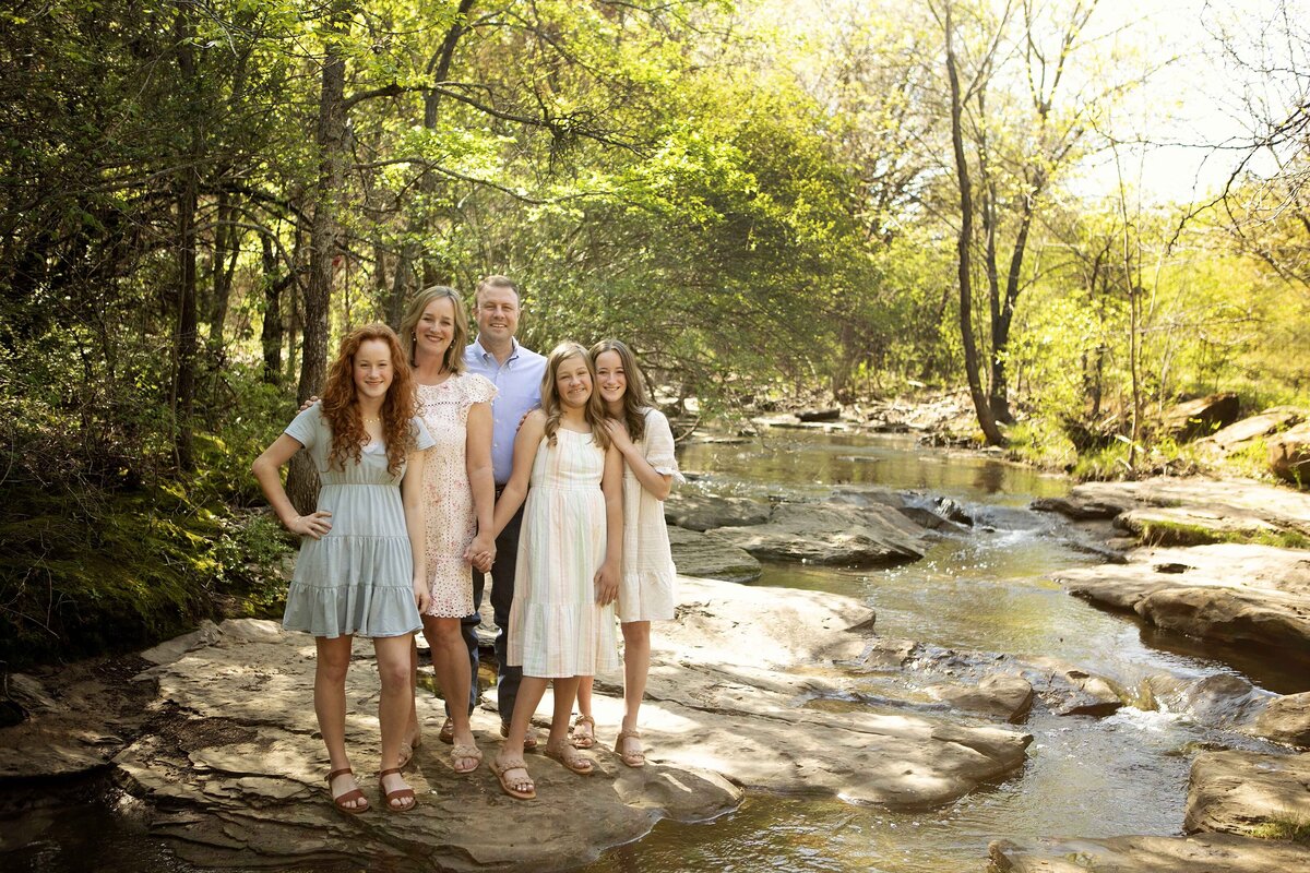 Parents and their three daughters standing near the creek, all laughing and enjoying a family photo session