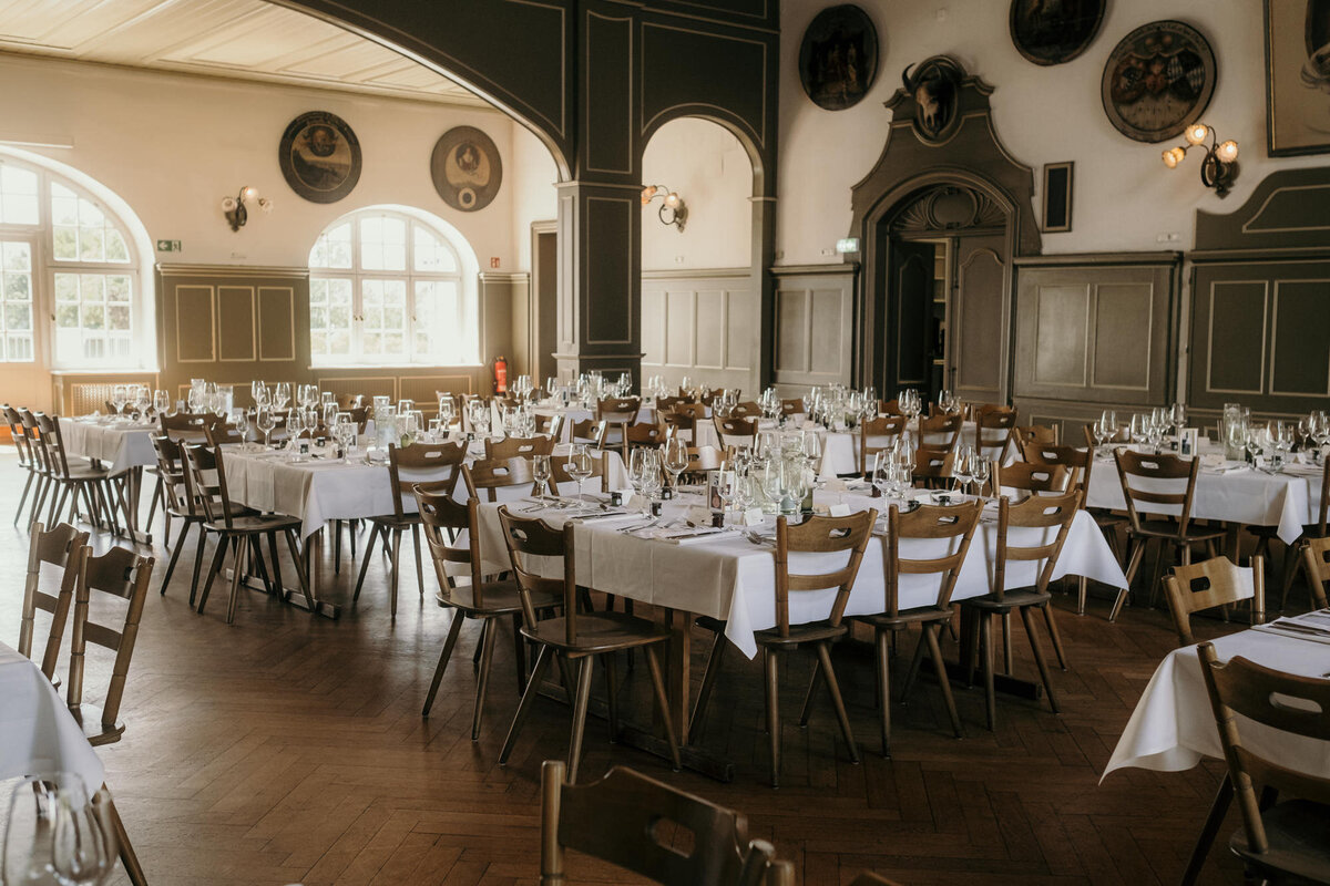Der Festsaal der Hochzeitslocation ist mit mehreren eckigen Tischen fertig eingedeckt für die Gäste.