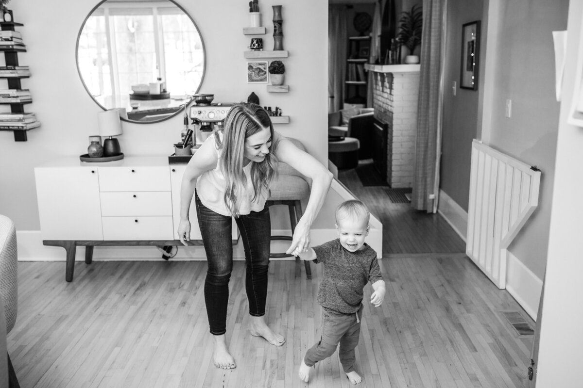 Black and white image of a mother playing and laughing with her toddler in a cozy living room.