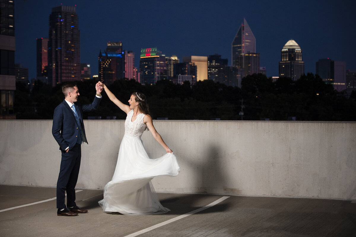 Nighttime portrait of a bride and groom dancing on a rooftop parking deck with the Charlotte city skyline in the background by Charlotte wedding photographers DeLong Photography