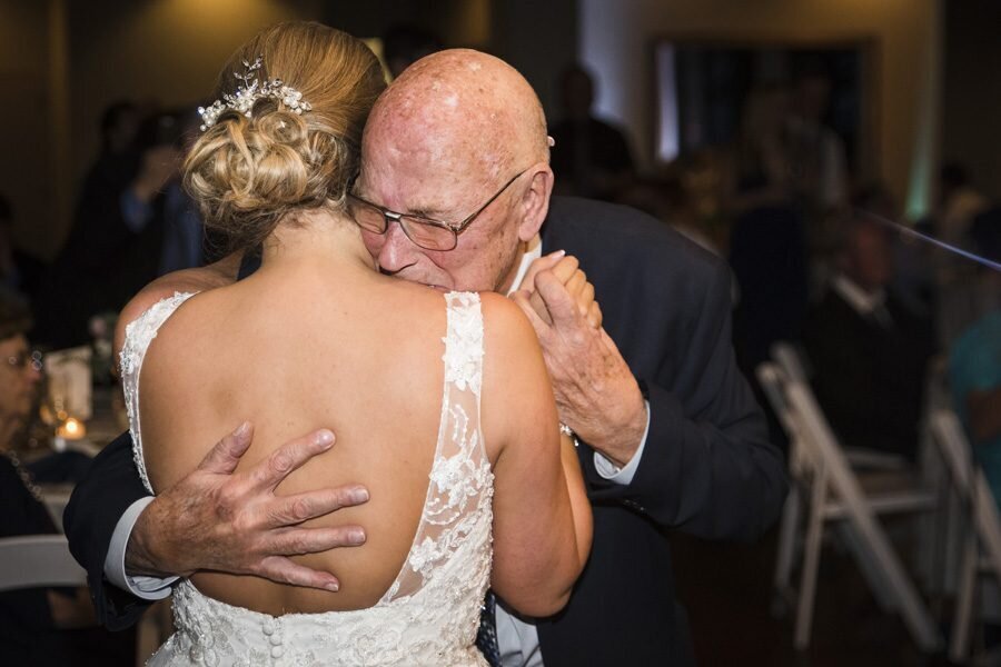 A father of the bride embraces his daughter as they share an emotional dance at their wedding reception.