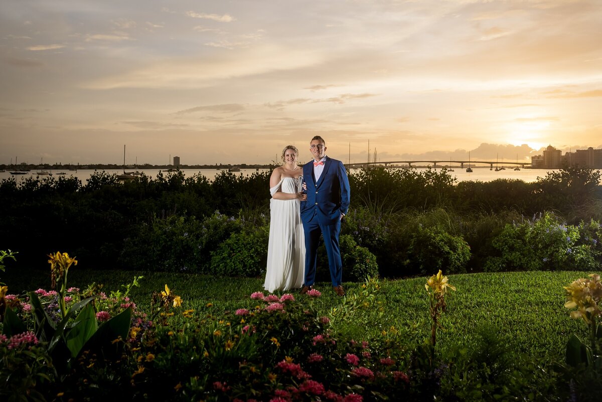 Bride and Groom in wedding attire at Selby Gardens with the Ringling bridge and sun setting in the background.