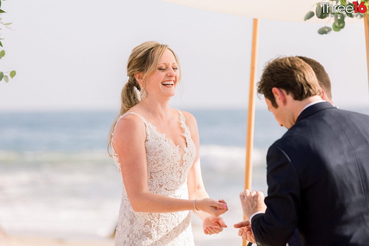 Bride laughs as the Groom fumbles with the wedding ring during the ceremony at the beach