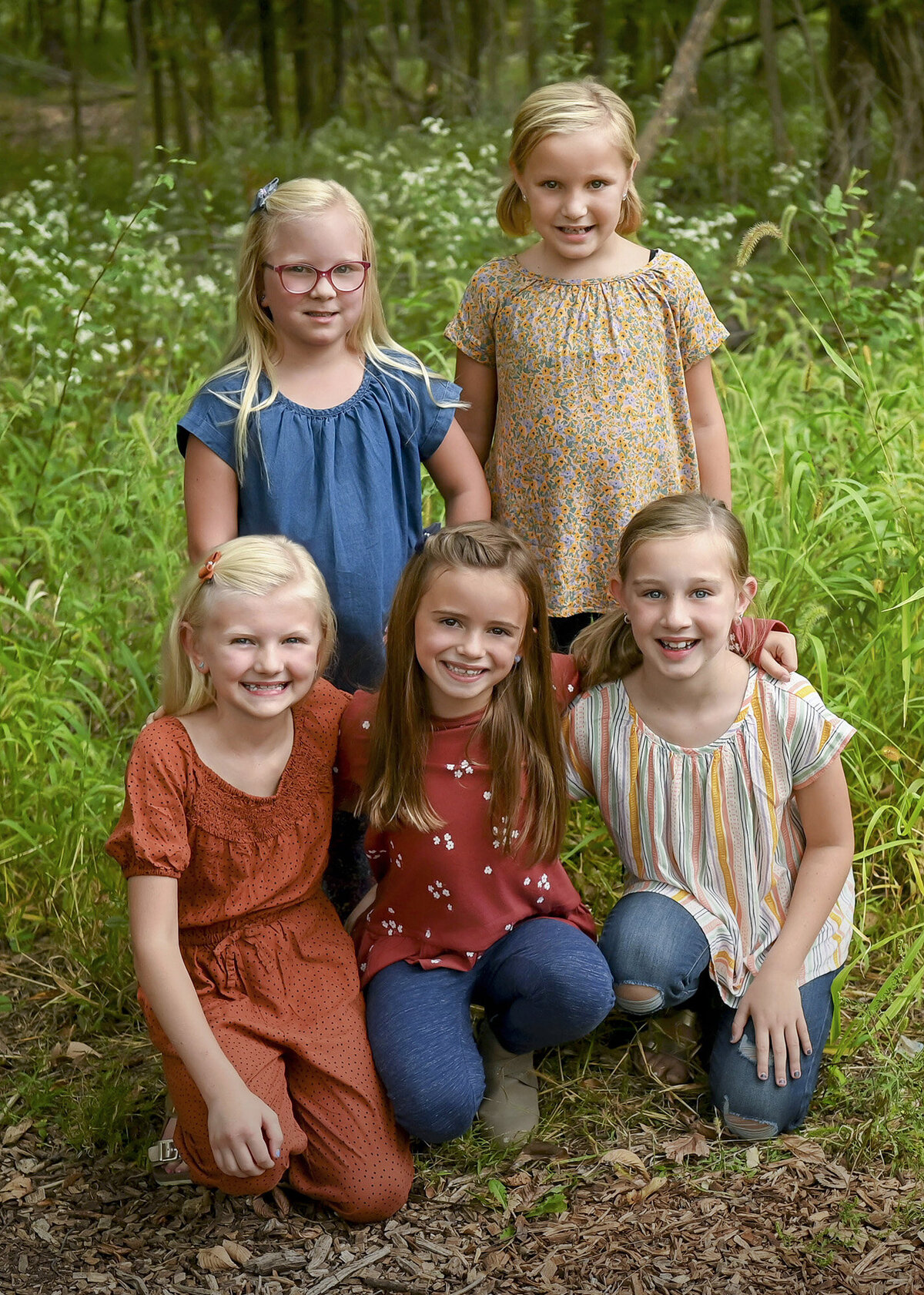 5 girls sit and stand together in a woodsy area
