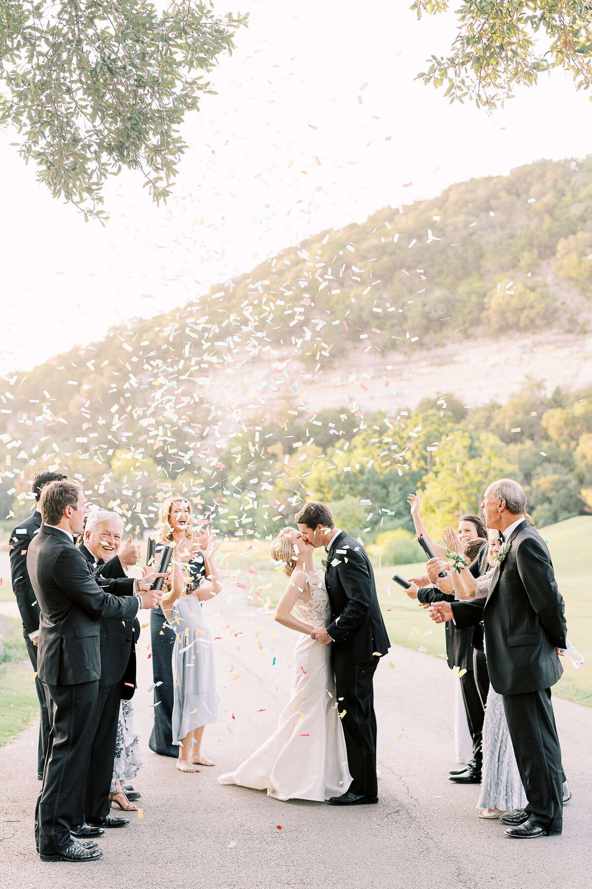 Bride and groom kiss with wedding party throwing confetti at Tapatio Springs Hill Country Resort