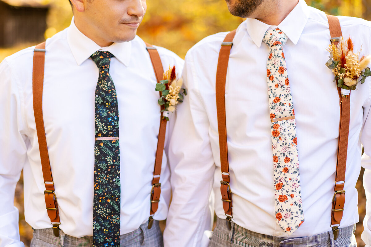 Two grooms in suspenders and floral ties look at each other lovingly at their wedding at Cuyahoga Falls, Ohio.