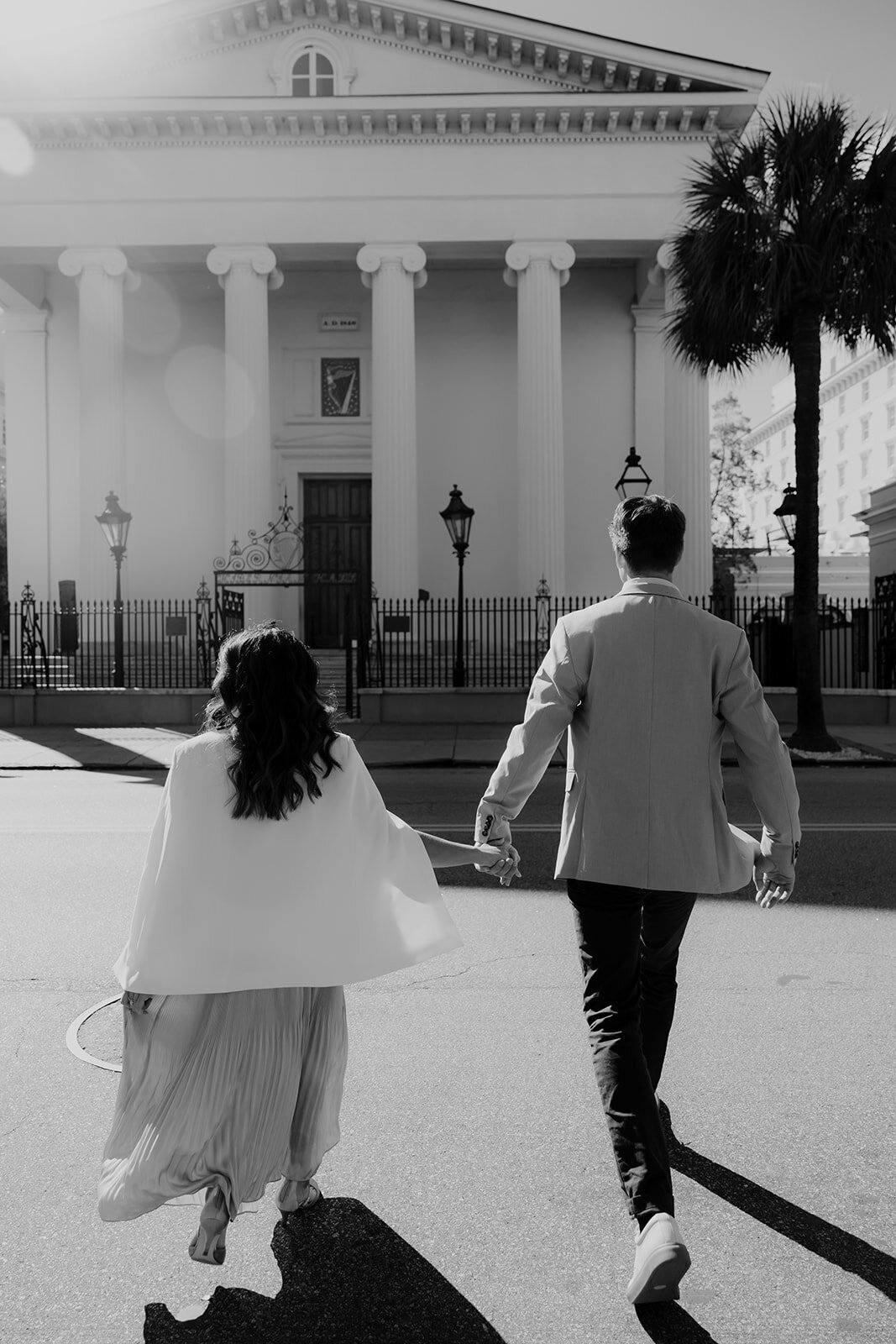 Couple crossing street and walking towards Hibernian Hall in Charleston for engagement photos