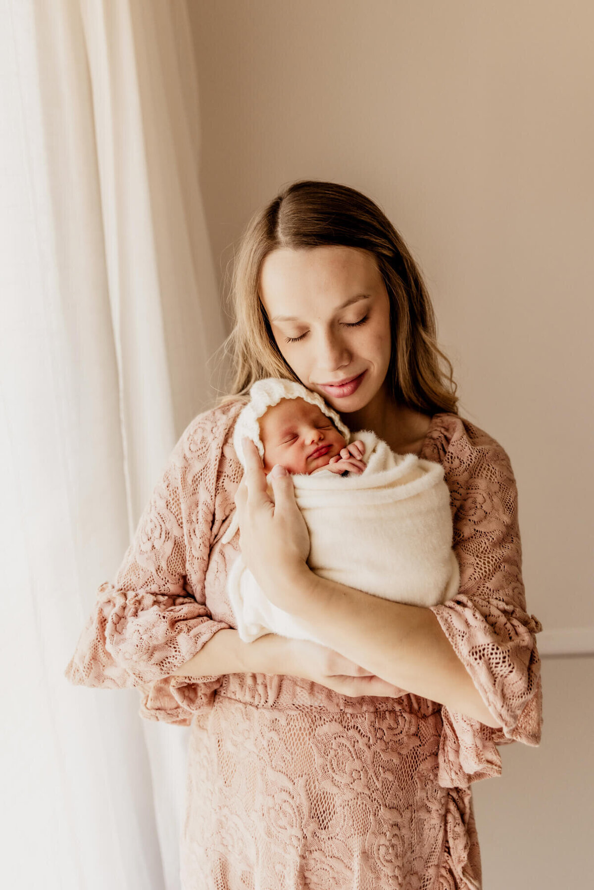 Mother with blonde hair holding her baby girl in her arms next to her cheek.