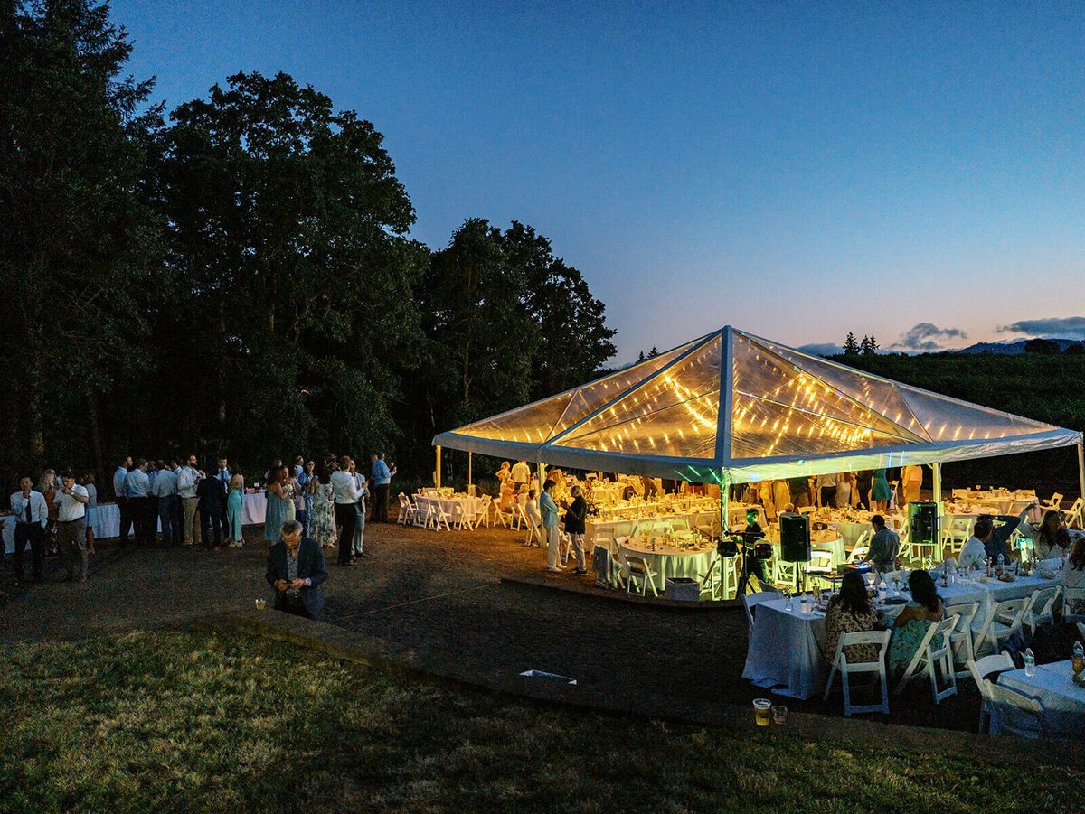A wedding reception tent lit up with string lights at night.