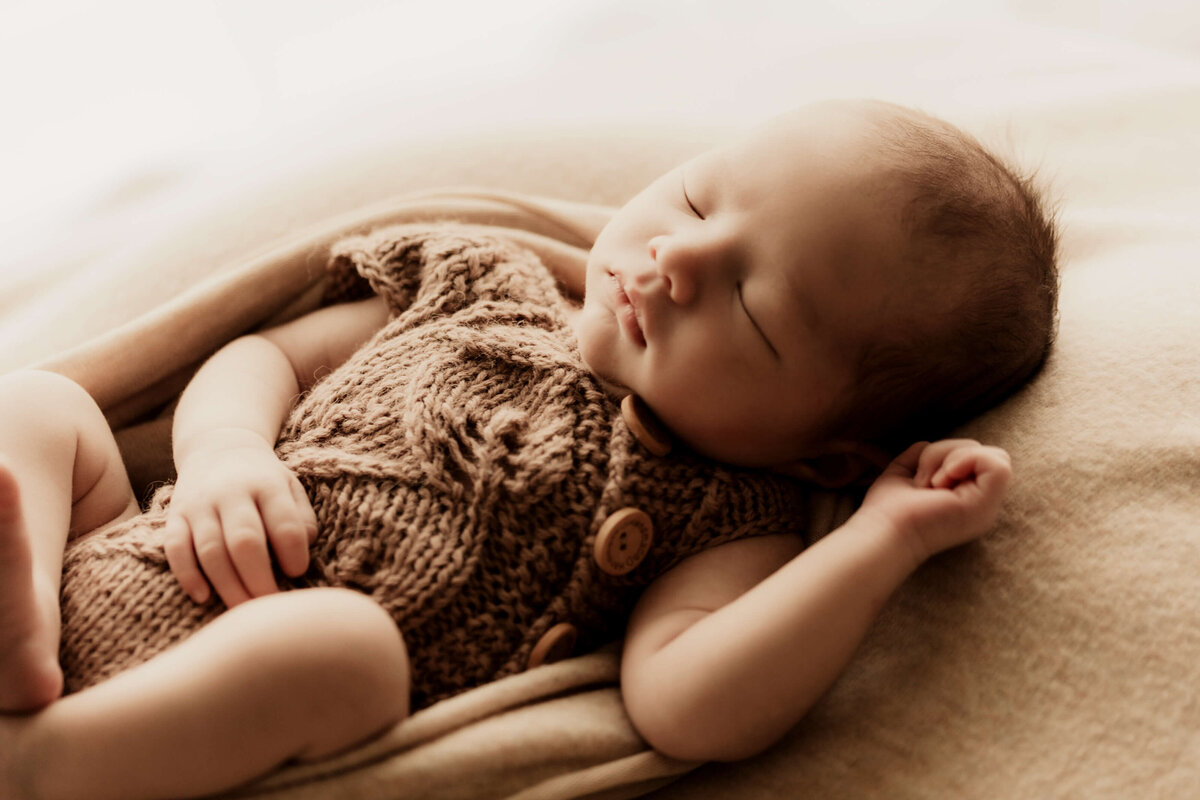 Newborn baby boy wearing a brown knit romper sleeping.