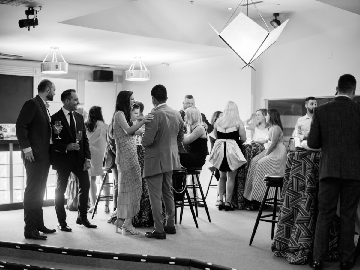 A vibrant social scene set in a chic bar, showcasing elegantly dressed guests enjoying drinks and engaging in lively conversations, creating an inviting atmosphere filled with laughter.
