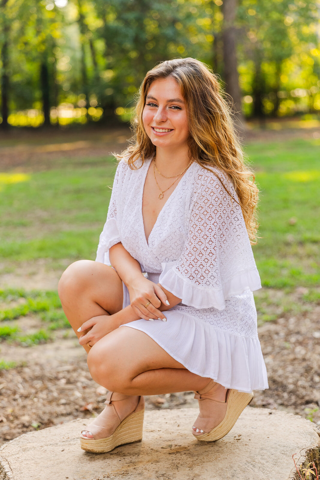 senior girl kneeling on a tree trunk one knee up sideway from the camera