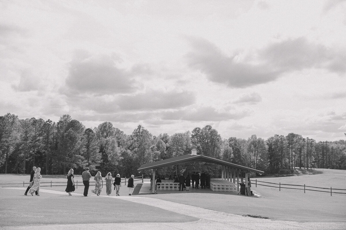 Candid black and white of wedding guests walking towards the ceremony site.