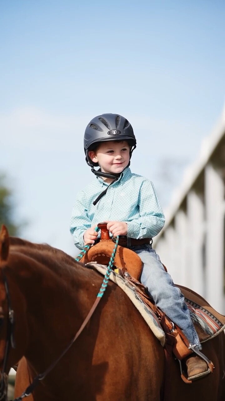 a young boy is riding in a western saddle, he is sitting on top of a chestnut horse