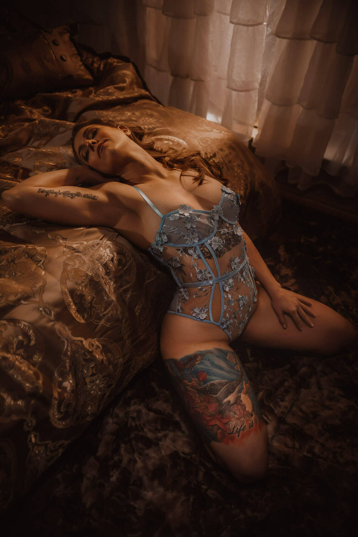 Woman in blue lace lingerie leaning back on a bed in a boudoir studio near DFW